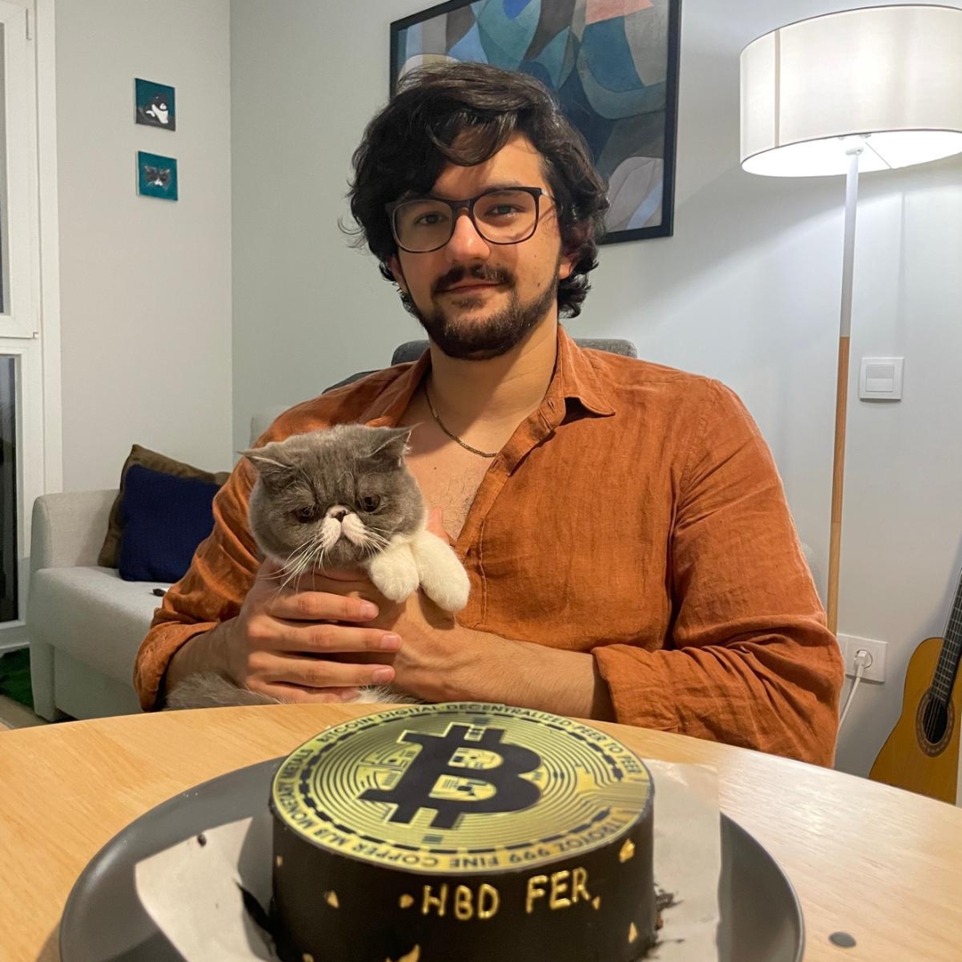 Fernando holding his cat next to a Bitcoin-themed birthday cake